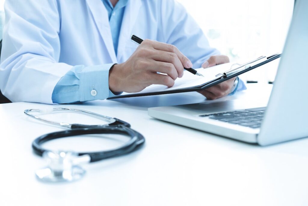 doctor working with laptop computer writing paperwork hospital background